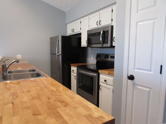 Kitchen featuring butcher block counter tops, white cabinets, double bay sink and stainless steel appliances. | Image 22