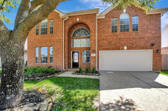 Charming two-story brick home with a spacious two-car garage, arched windows, and a welcoming front entrance. The well-maintained front yard features mature trees and landscaped greenery. | Image 5