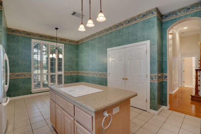 Kitchen with white appliances, wallpapered walls, light tile patterned floors, arched walkways, and light countertops | Image 13