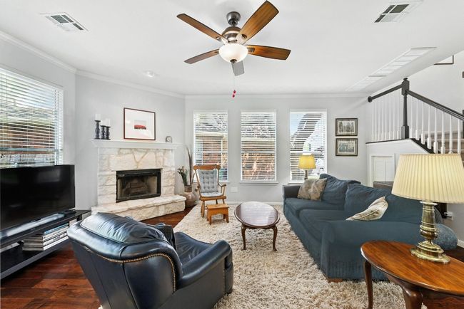 Living area with a ceiling fan, crown molding, wood finished floors, a stone fireplace, and stairs | Image 5