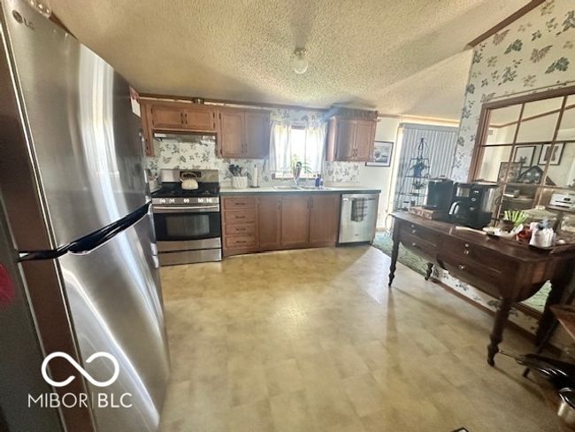 kitchen featuring wallpapered walls, under cabinet range hood, light floors, a textured ceiling, and appliances with stainless steel finishes | Image 8
