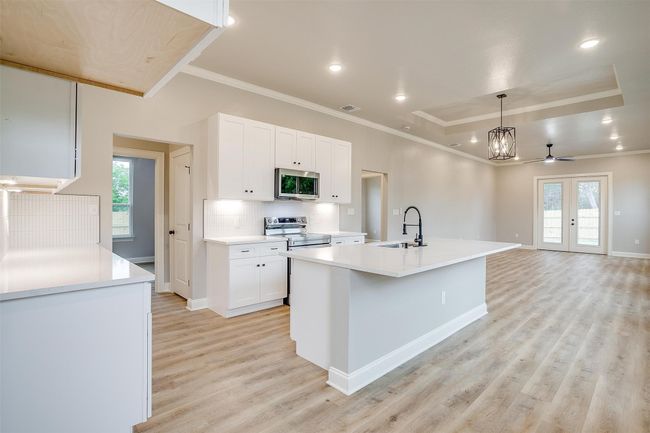 Kitchen with white cabinets, a sink, light wood finished floors, plenty of natural light, and stainless steel appliances | Image 12