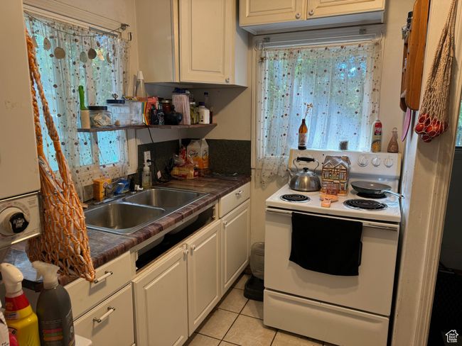 Kitchen with white cabinets, dark countertops, light tile patterned floors, a sink, and electric range | Image 9