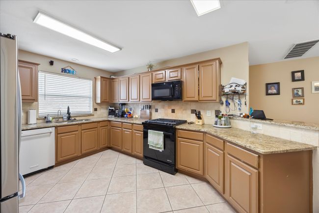 Kitchen with black appliances, a sink, a peninsula, backsplash, and light tile patterned floors | Image 11