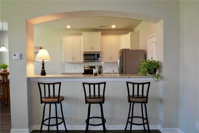 Kitchen featuring stainless steel appliances, arched walkways, backsplash, a peninsula, and light stone counters | Image 4