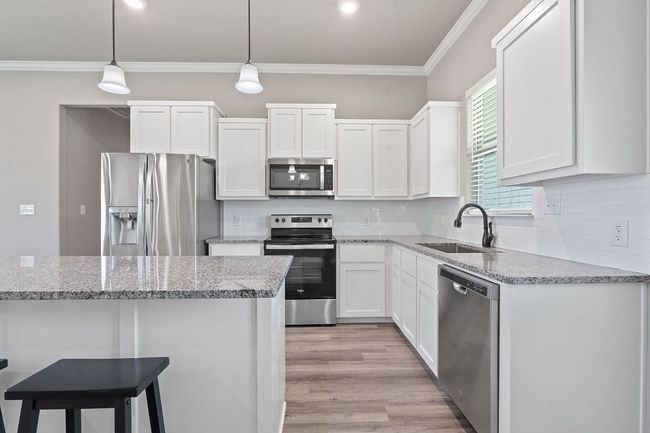 Kitchen featuring appliances with stainless steel finishes, white cabinets, ornamental molding, tasteful backsplash, and pendant lighting | Image 12