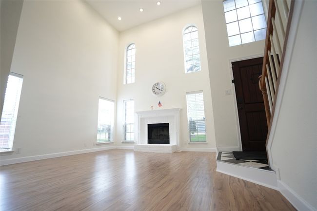 Unfurnished living room with wood finished floors, plenty of natural light, a fireplace, recessed lighting, and a towering ceiling | Image 7