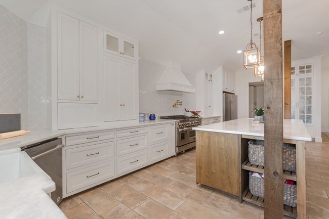 Kitchen with premium appliances, custom exhaust hood, decorative backsplash, light countertops, and white cabinets | Image 13