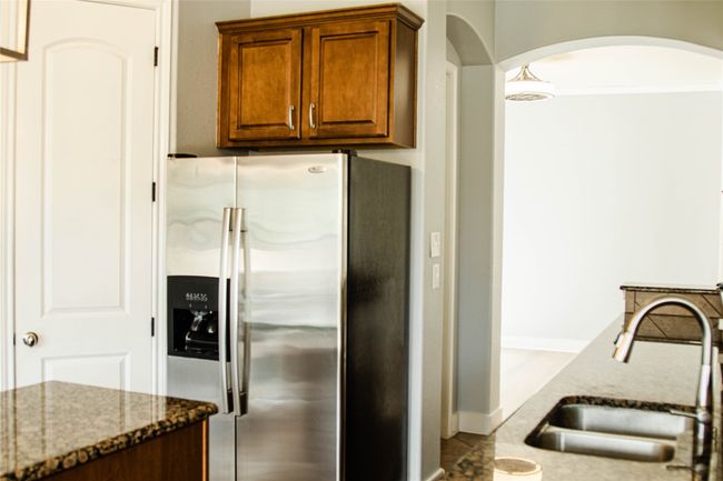 Kitchen with stainless steel refrigerator with ice dispenser, arched walkways, dark stone counters, and brown cabinetry | Image 7