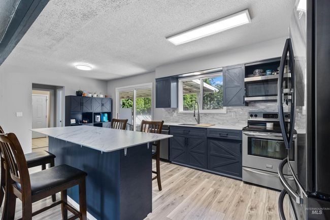 Kitchen featuring stainless steel appliances, a kitchen breakfast bar, light wood finished floors, tasteful backsplash, and a textured ceiling | Image 12