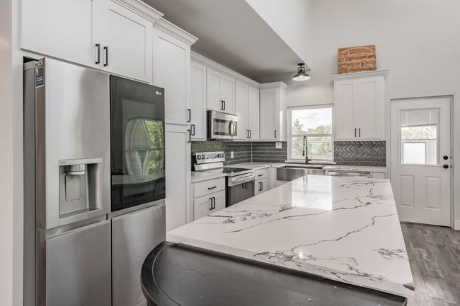 Kitchen featuring stainless steel appliances, a sink, backsplash, white cabinetry, and a center island | Image 25