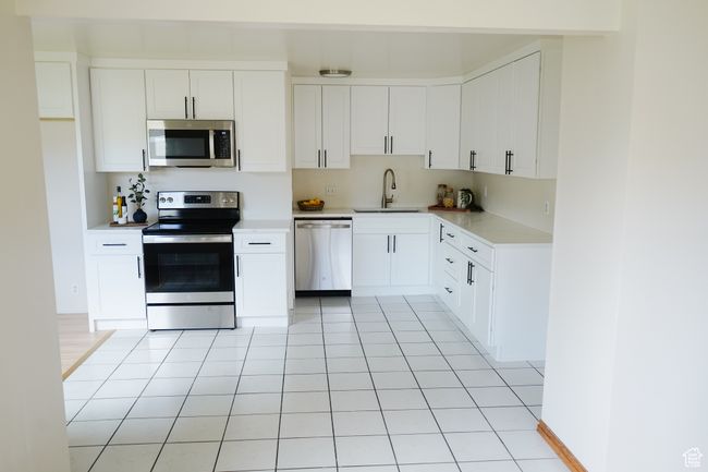 Kitchen featuring stainless steel appliances, light tile patterned flooring, light countertops, and white cabinetry | Image 5