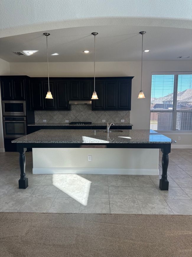Kitchen featuring an island with sink, dark stone countertops, pendant lighting, and backsplash | Image 9