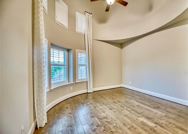 This room features high ceilings with a ceiling fan, elegant hardwood flooring, and large windows with plantation shutters and long drapes, allowing plenty of natural light. The curved wall adds a unique architectural touch. | Image 41