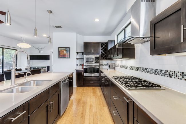 Kitchen with sink, dark brown cabinetry, decorative light fixtures, stainless steel appliances, and wall chimney exhaust hood | Image 9