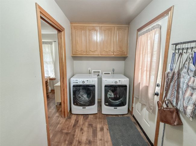Clothes washing area featuring a healthy amount of sunlight, wood finished floors, cabinet space, and washing machine and clothes dryer | Image 21