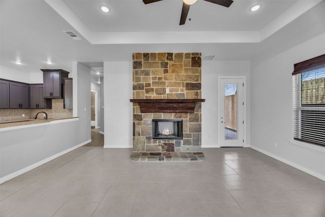 Unfurnished living room with ceiling fan, light tile patterned floors, a fireplace, and a tray ceiling | Image 10