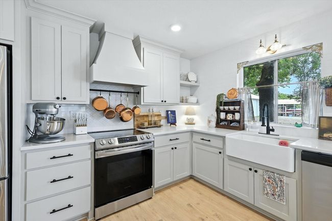 Kitchen featuring stainless steel appliances, light wood finished floors, custom range hood, light countertops, and backsplash | Image 14
