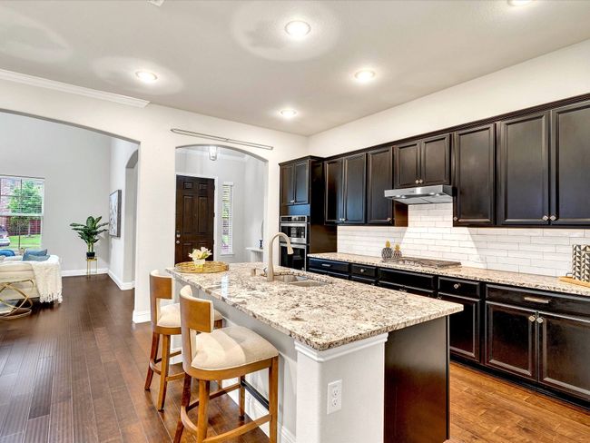 Kitchen with arched walkways, a kitchen breakfast bar, light stone countertops, backsplash, and a center island with sink | Image 10