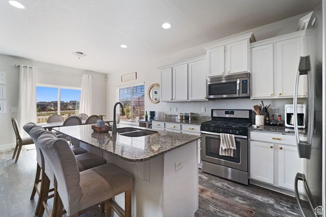 Kitchen with dark wood finished floors, dark stone counters, appliances with stainless steel finishes, a sink, and a center island with sink | Image 5
