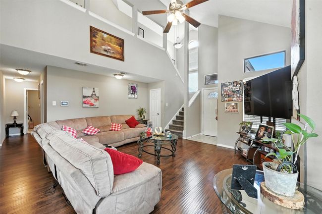 Living area featuring a high ceiling, a ceiling fan, stairway, and wood finished floors | Image 10