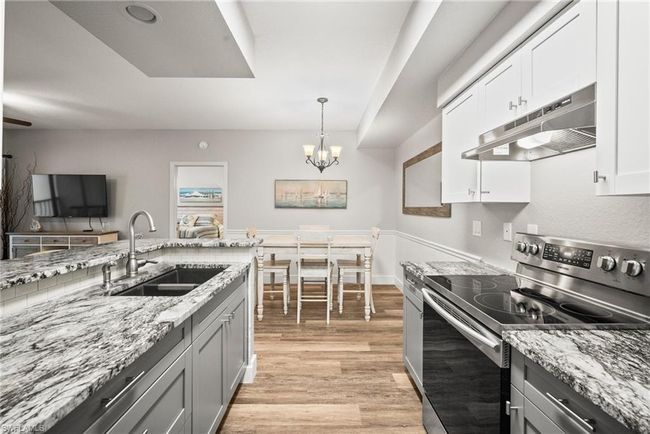 Kitchen with a sink, a chandelier, light wood finished floors, under cabinet range hood, and electric stove | Image 24