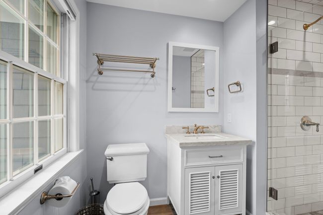 The en suite bathroom showcases a modern design with a marble vanity, brushed gold fixtures, and a frameless glass shower surrounded by crisp white subway tile. | Image 27