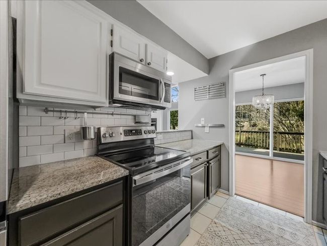 Kitchen with light stone countertops, appliances with stainless steel finishes, white cabinets, and backsplash | Image 12