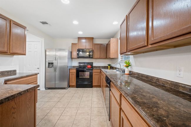 Kitchen with a sink, dark stone countertops, visible vents, black appliances, and light tile patterned floors | Image 7