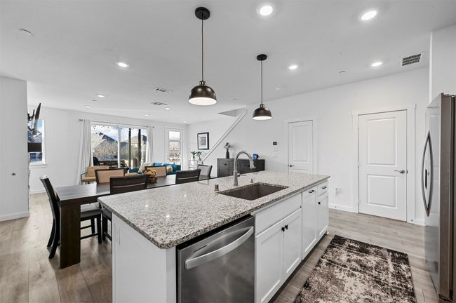 Kitchen with sink, white cabinetry, stainless steel appliances, a center island with sink, and decorative light fixtures | Image 5