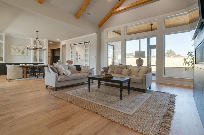 Living room with beam ceiling, a barn door, high vaulted ceiling, a chandelier, and light wood-type flooring | Image 6