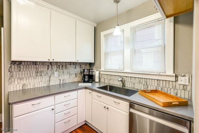 Kitchen featuring stainless steel dishwasher, hanging light fixtures, a sink, decorative backsplash, and white cabinets | Image 15