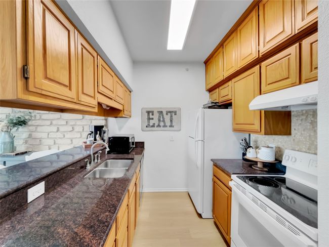 Kitchen featuring white appliances, under cabinet range hood, a sink, backsplash, and light wood-style floors | Image 13