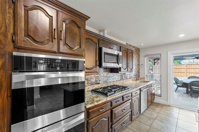 Kitchen featuring light stone countertops, a sink, tasteful backsplash, dark brown cabinetry, and appliances with stainless steel finishes | Image 22
