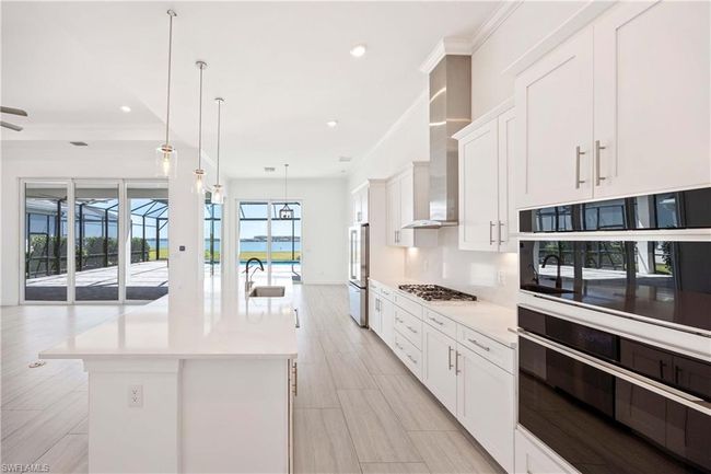 Kitchen with white cabinetry, light countertops, stainless steel appliances, and an island with sink | Image 10