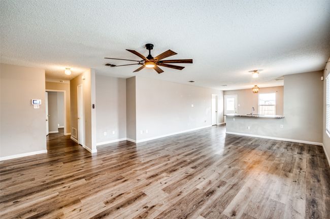 Unfurnished living room featuring a textured ceiling, wood finished floors, ceiling fan, and baseboards | Image 4
