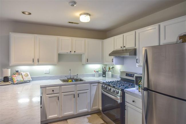 Kitchen with stainless steel appliances, a sink, under cabinet range hood, light countertops, and recessed lighting | Image 7