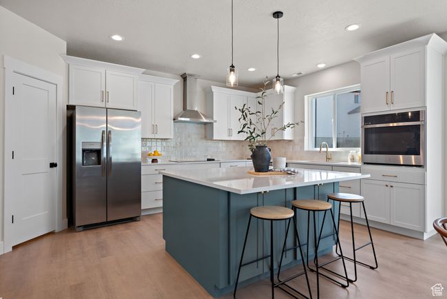 Kitchen featuring stainless steel appliances, wall chimney exhaust hood, light wood-style flooring, white cabinetry, and tasteful backsplash | Image 10