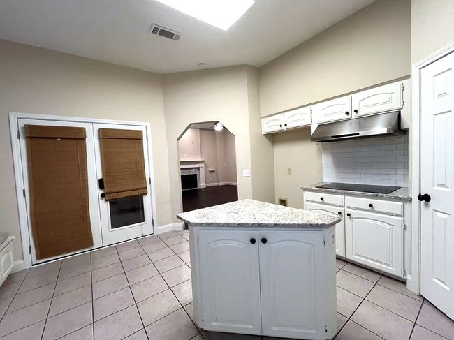 Kitchen with under cabinet range hood, light tile patterned flooring, black electric stovetop, a center island, and white cabinets | Image 15