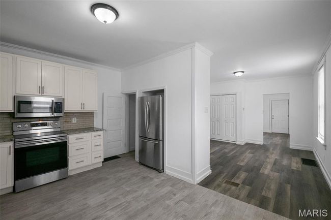 Kitchen featuring stainless steel appliances, decorative backsplash, ornamental molding, dark wood-type flooring, and light stone countertops | Image 8