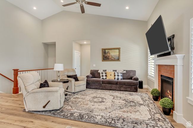 Living room featuring high vaulted ceiling, a ceiling fan, wood finished floors, a glass covered fireplace, and recessed lighting | Image 7