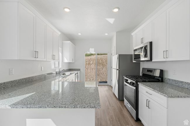Kitchen with white cabinets, a sink, appliances with stainless steel finishes, light wood finished floors, and light stone counters | Image 4
