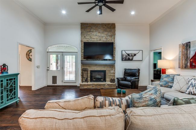 Living room with high ceilings, ornamental molding, a ceiling fan, a stone fireplace, and Luxury Vinyl Flooring through out | Image 6