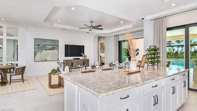 Kitchen featuring a ceiling fan, a tray ceiling, light stone counters, white cabinetry, and a kitchen island | Image 10