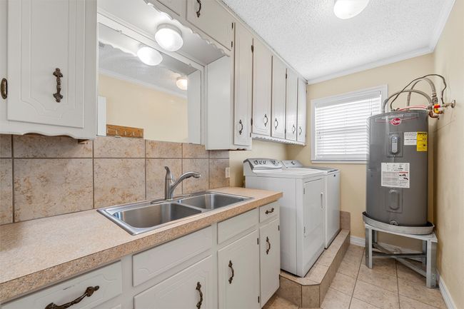 Laundry room with electric water heater, washing machine and dryer, ornamental molding, a textured ceiling, and cabinet space | Image 15