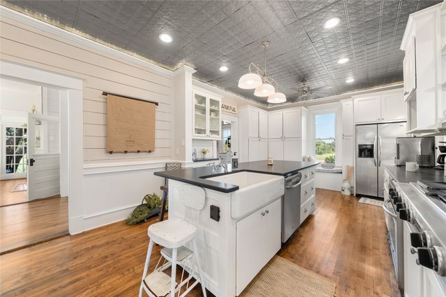 Kitchen featuring appliances with stainless steel finishes, wood finished floors, a kitchen island with sink, white cabinetry, and an ornate ceiling | Image 8