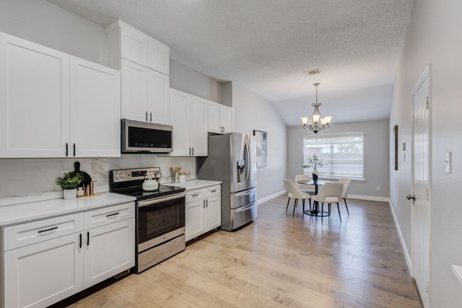 Kitchen with appliances with stainless steel finishes, a chandelier, vaulted ceiling, white cabinetry, and light wood finished floors | Image 7