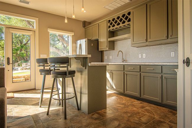 Kitchen featuring stone tile floors, gray cabinetry, a kitchen bar, and tasteful backsplash | Image 31