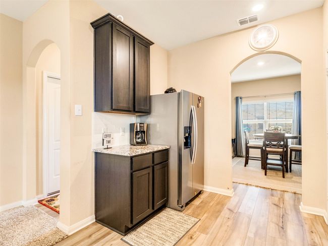 Kitchen featuring light stone counters, stainless steel fridge with ice dispenser, dark brown cabinets, light hardwood / wood-style flooring, and backsplash | Image 10