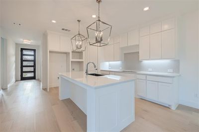 Kitchen with light hardwood / wood-style floors, an island with sink, white cabinets, an inviting chandelier, and decorative light fixtures | Image 3